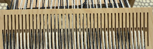 Wooden loom with black and white threads woven through slots. A polka dot fabric is visible in the blurred background.