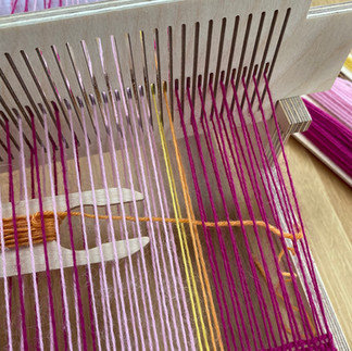 an orange weft thread being woven into the weave of a rigid heddle loom