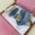 A crafting kit with blue and white yarn on wooden spools, paper instructions, and a pink lining, presented in an open cardboard box.