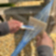 Hands weaving blue threads using a wooden loom against a wooden fence background. Threads fan out with a focus on the weaving process.