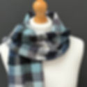 A mannequin wooden head displays a blue, gray, and black plaid scarf against a dark gray background, creating a cozy, elegant mood.