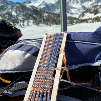 a blue and orange weaving on a bookmark weaving loom laid on a bag in a ski resort