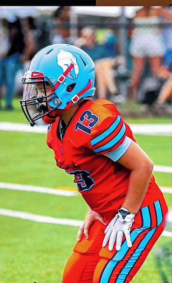 "Pop Warner football player in full uniform catching a football on a wet field, illustrating youth athletes benefiting from Game Ready Football Prep’s prepped game balls for improved grip and performance."