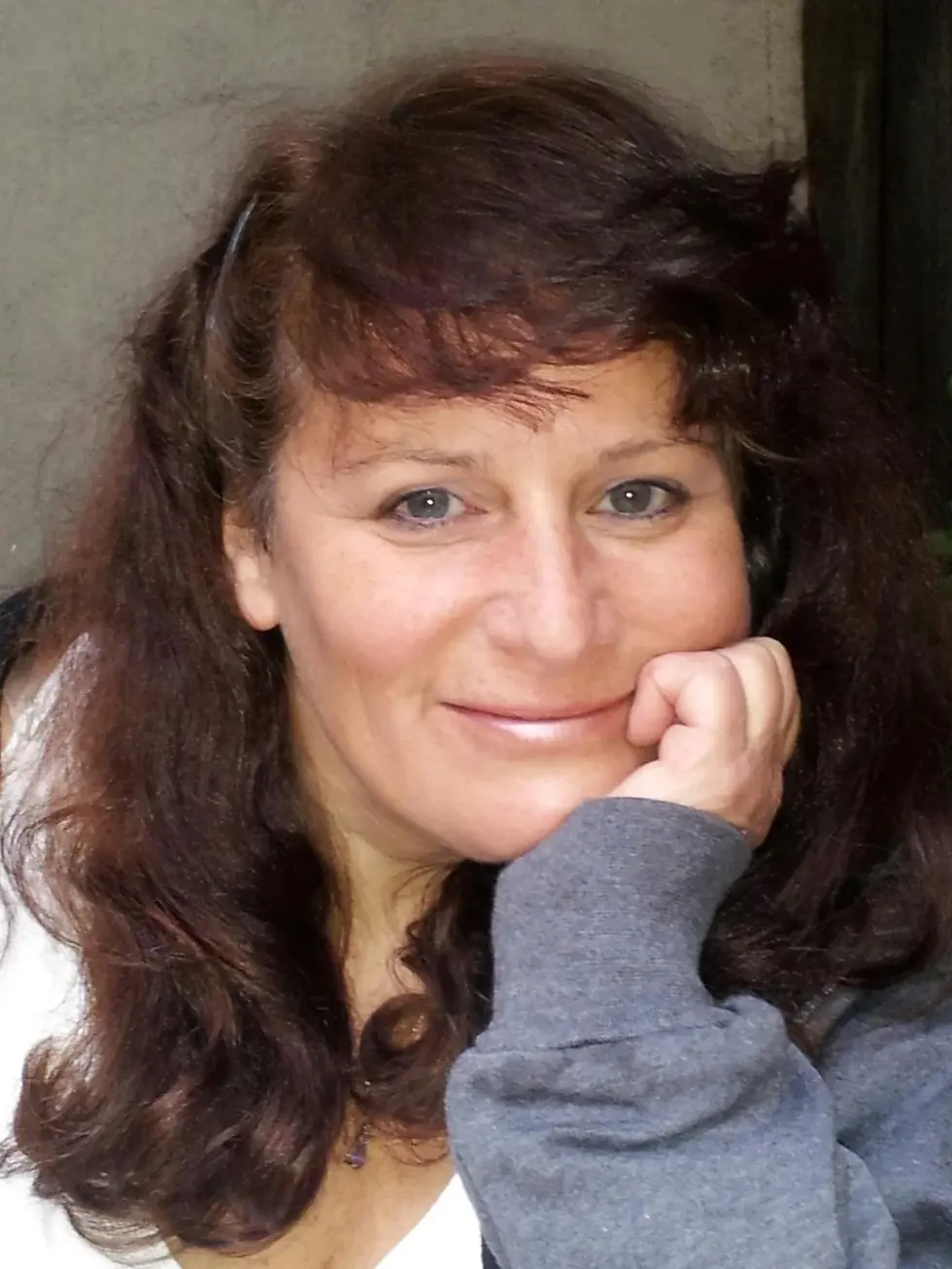 Portrait of a woman with long wavy brown hair resting her chin on her hand, smiling at the camera, vertical orientation