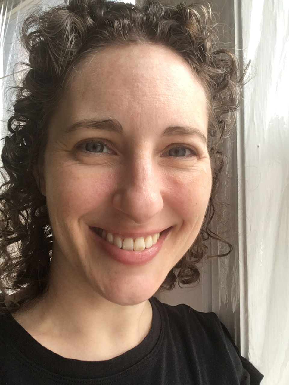 Portrait photo of a smiling adult facing the camera, close-up, natural indoor light, portrait orientation.