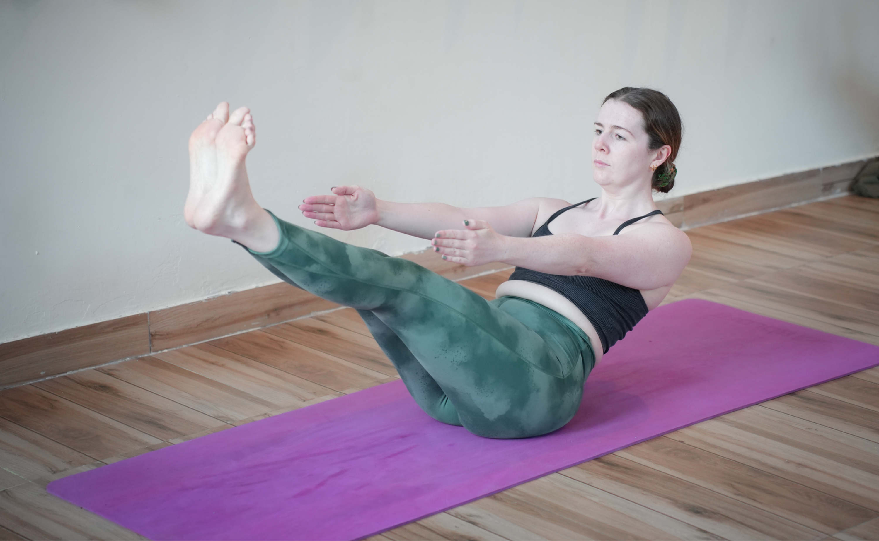 Yoga student doing boat pose where there feet are lifted, their core is engaged, they are sitting at a 45 degree angle and their arms are reaching forward