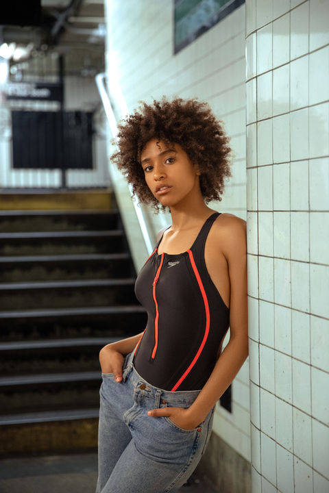 a woman in a speedo swimsuit leans against a wall