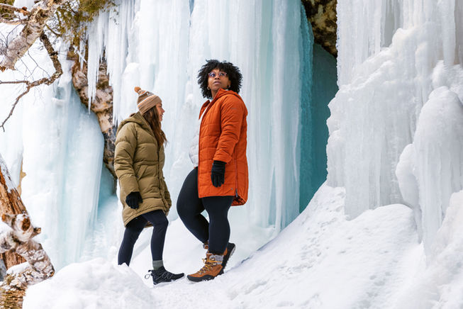 two women standing in front of a frozen waterfall