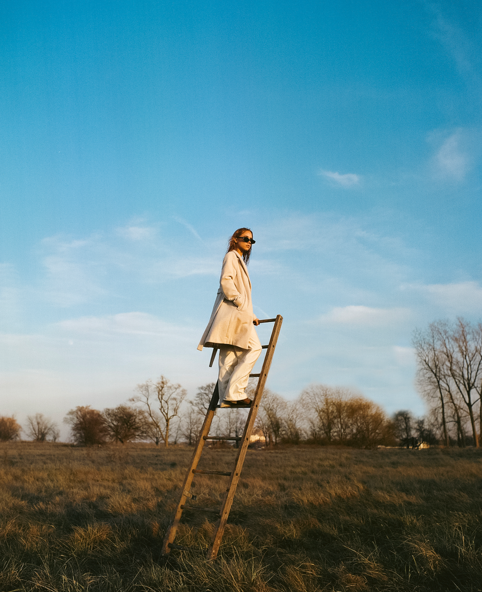 a woman stands on a wooden ladder in a field