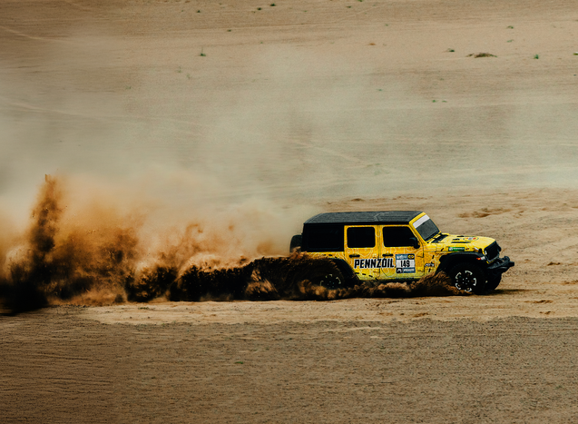 a yellow pennzoil jeep is driving through the dirt
