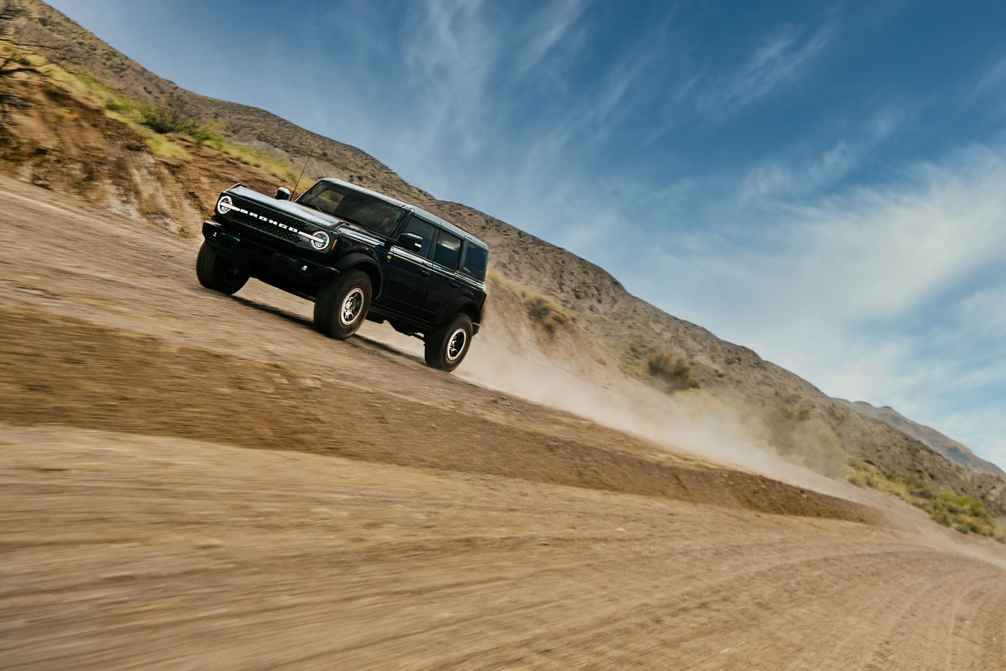 a black ford bronco is driving down a dirt road