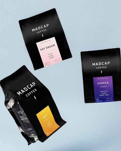 three bags of madcap coffee sit on a blue surface