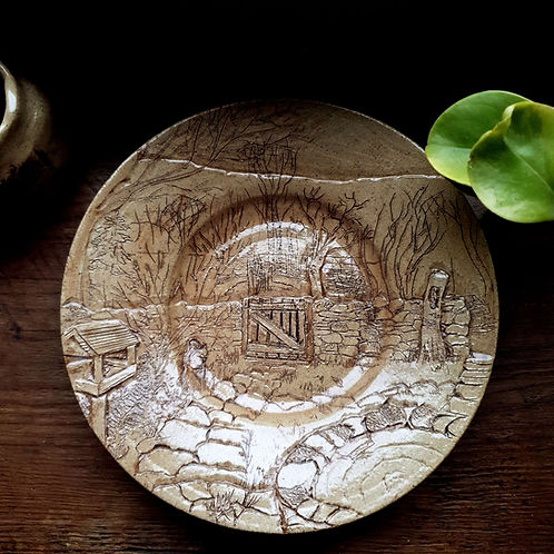 Plate with wide rim illustrated all over with a garden scene featuring a gate in the middle, pond and squirrel.