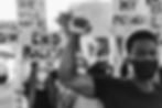 Protesters with fists raised; a man in a mask stands in front. Signs read "End Racism." The mood is determined and unified. Black and white image.