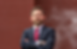 Elijah Bergman in a suit with arms crossed against a brick wall.