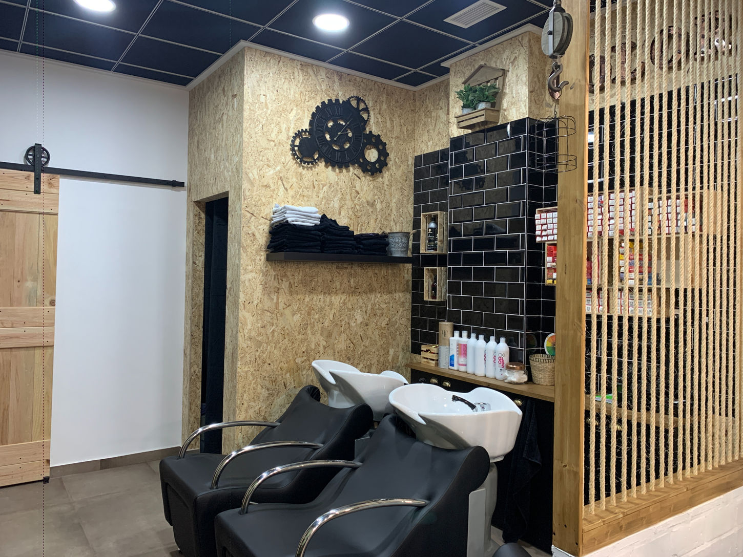 Zona de lavado en peluquería con sillones reclinables y revestimiento industrial diseñada por Genovés Calleja Arquitectos.
