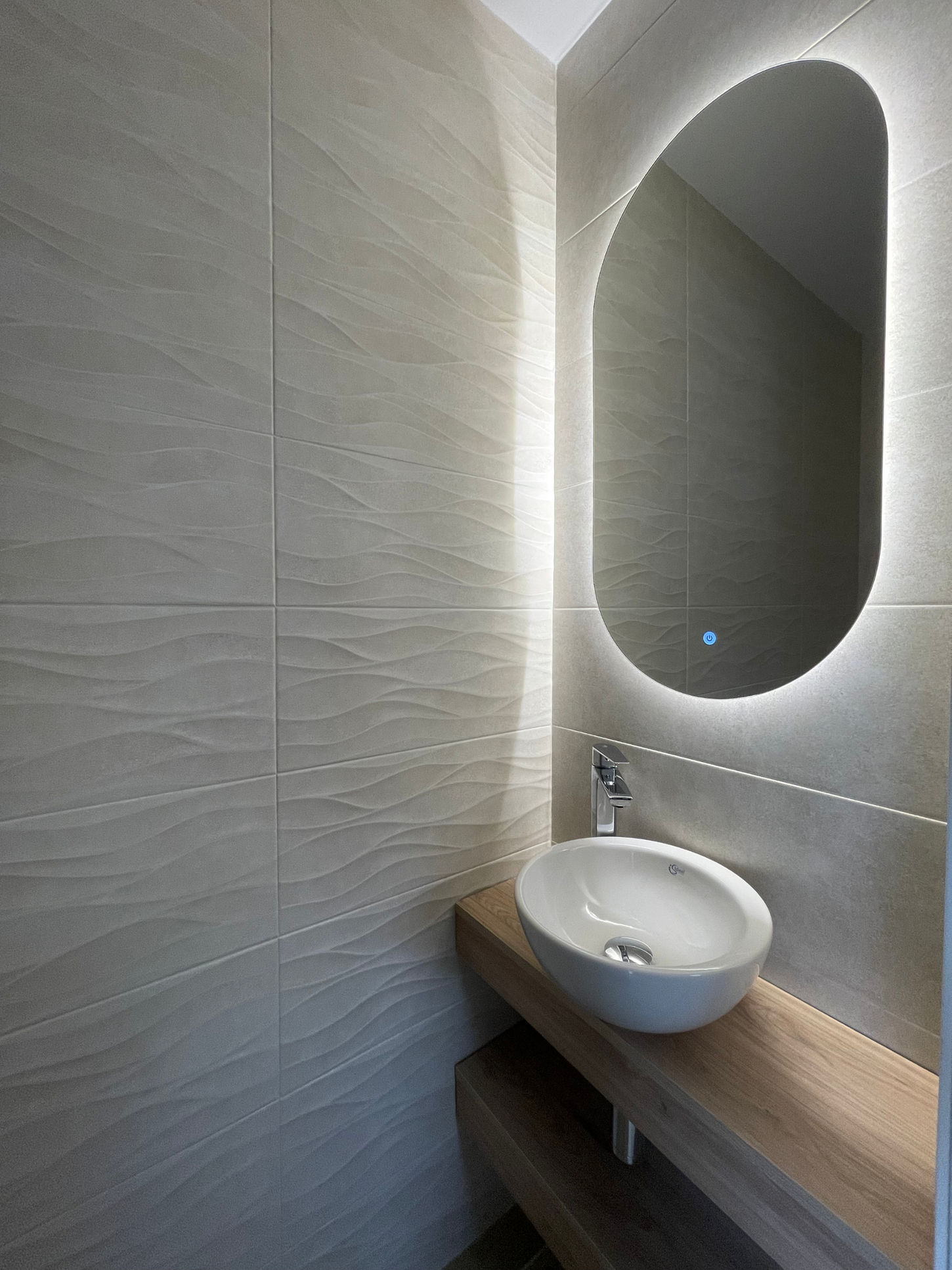 Aseo moderno con lavabo sobre encimera de madera y espejo retroiluminado en vivienda unifamiliar diseñada por Genovés Calleja Arquitectos.