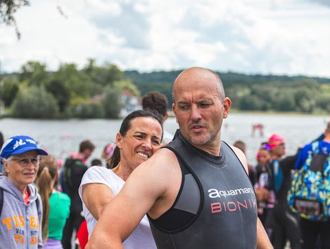 Une femme aide un homme à mettre sa combinaison de plongée au bord de l'eau.
