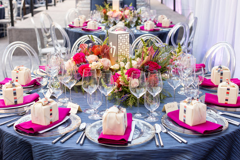 Glamorous round gala table with vivid floral arrangement, ghost chairs, and personalized table cards.