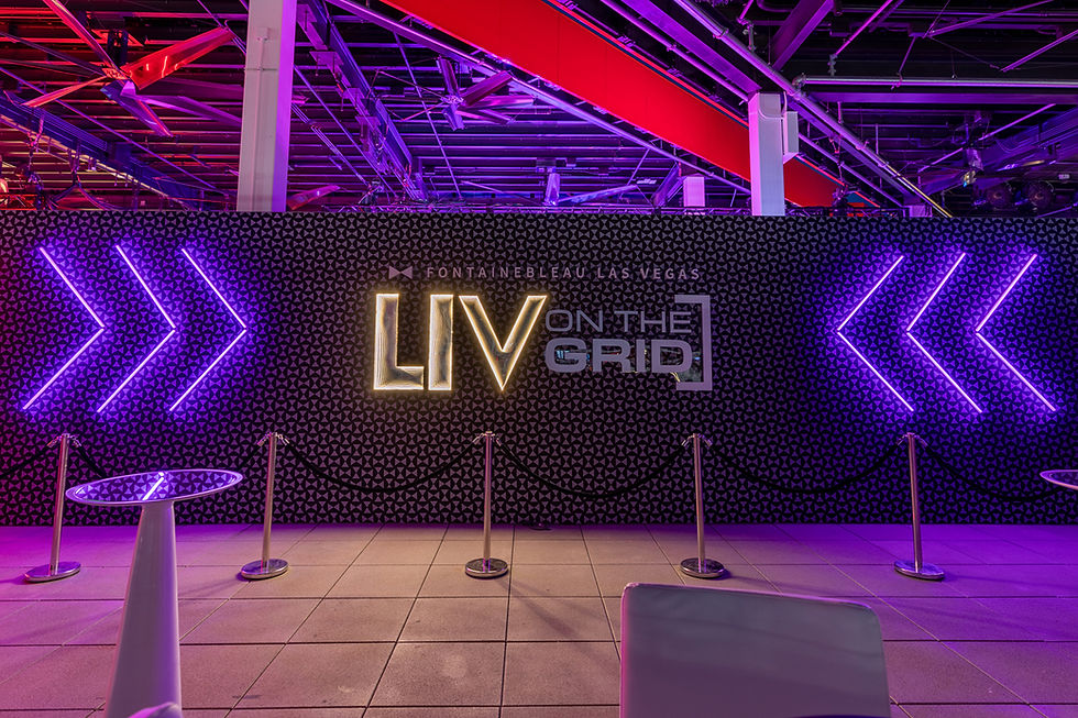 Neon-lit "LIV On The Grid" sign with purple arrows, black patterned backdrop, and ropes in Fontainebleau Las Vegas. Vibrant, futuristic feel.