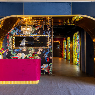 A lavish entranceway with gold arches, floral wallpaper, and a plush red reception desk, leading into a glowing corridor at Papi Steak Las Vegas.