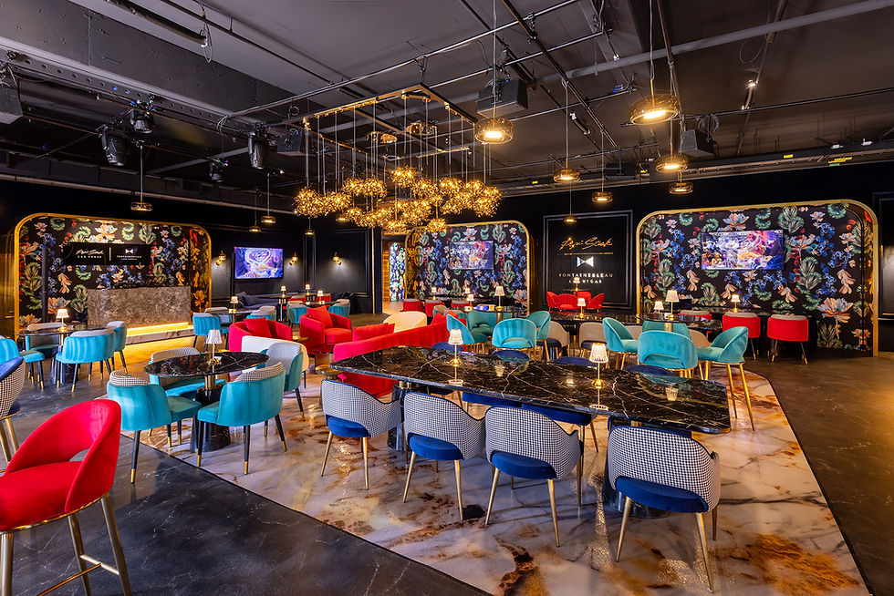 Chic lounge with vibrant red, blue chairs, black marble tables, and floral walls. Decorative lighting above. Text on walls, modern ambiance.