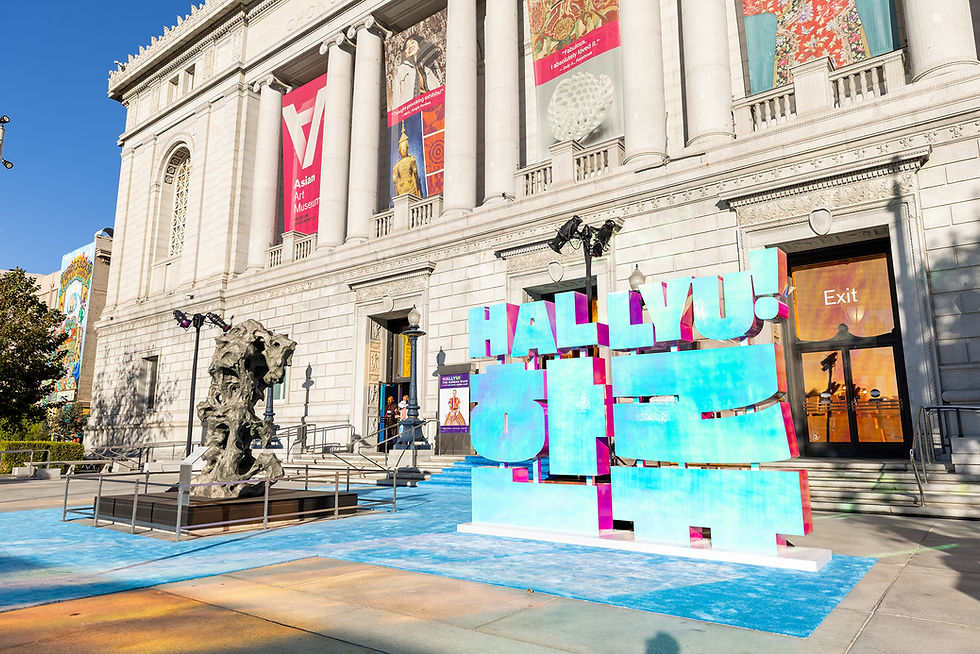 Exterior of Asian Art Museum in daylight with colorful "Hallyu!" sign and abstract sculpture. Vibrant banners hang on the building.