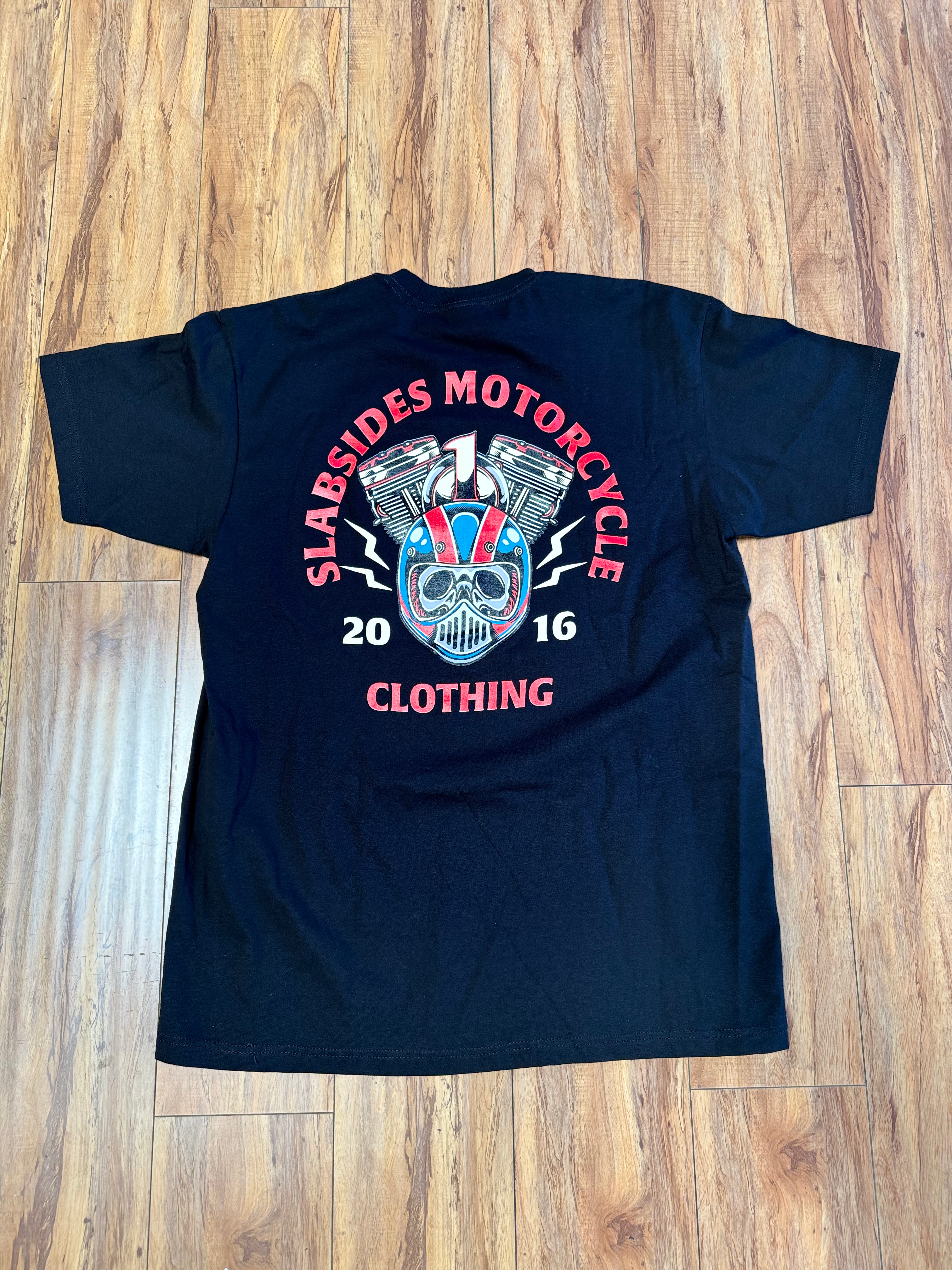 Black HELMET graphic T-shirt laid flat, featuring a bold front design across the chest, available in multiple sizes
