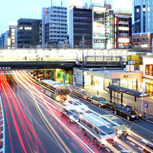paysage urbain à la tombée du jour montrant les éclairages jaunes et rouges des phares aitomobiles filant sous une gare de métro aérienne