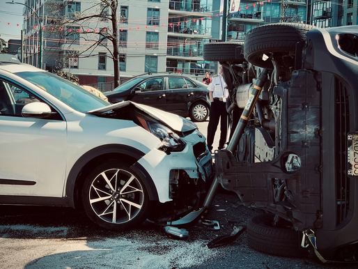 White SUV smashed into black sedan overturned on city street; debris scattered, police and bystanders nearby.