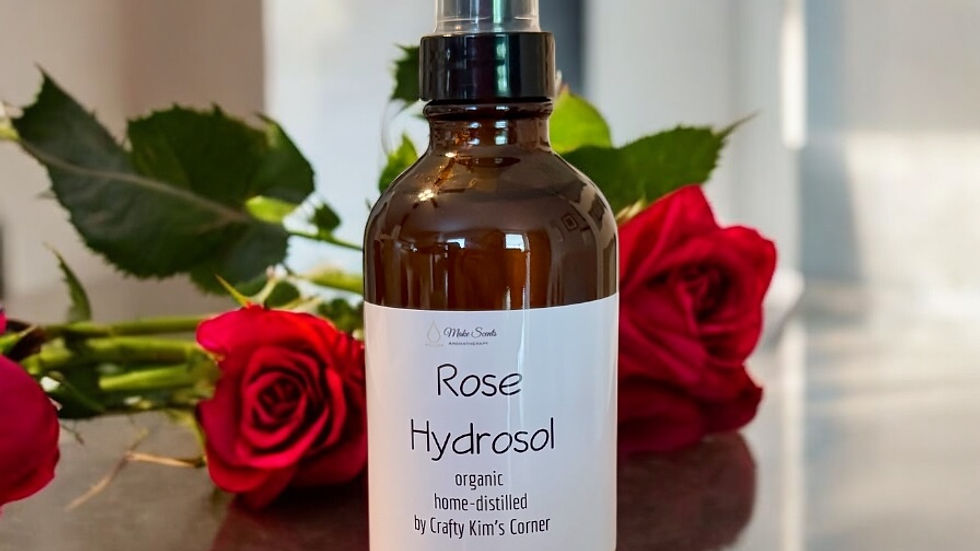 Brown bottle labeled "Rose Hydrosol" surrounded by red roses on a reflective surface; soft natural light in a minimal setting.