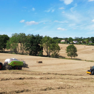 Field with rows of straw with two tractors in in with balers on baling straw