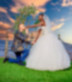 Groom kissing bride's hand at sunset by the lake