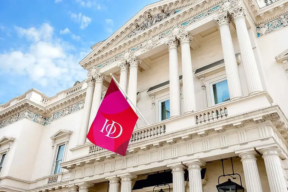 Institute of Directors — 116 Pall Mall. A Neoclassical building with white columns and ornate details. A red flag with "IoD" text waves in front, set against a blue sky.
