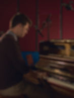 Charlie sits at a piano in a recording studio, mic'd up, recording music.