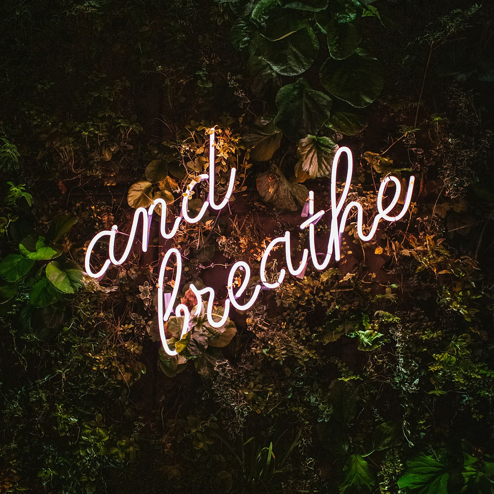 Neon sign reading "and breathe" glows against a lush green foliage background, creating a calming and serene atmosphere.
