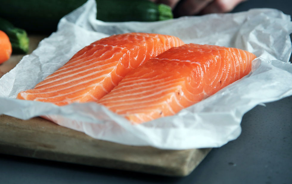 Two raw salmon fillets on parchment paper, resting on a wooden board. Background includes vegetables, evoking a fresh, kitchen setting. Salmon reduces inflammation