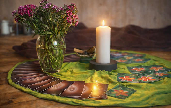 Eine Kerze mit Orakelkarten und Blumenstrauß auf dem Boden im Kreis dekoriert.