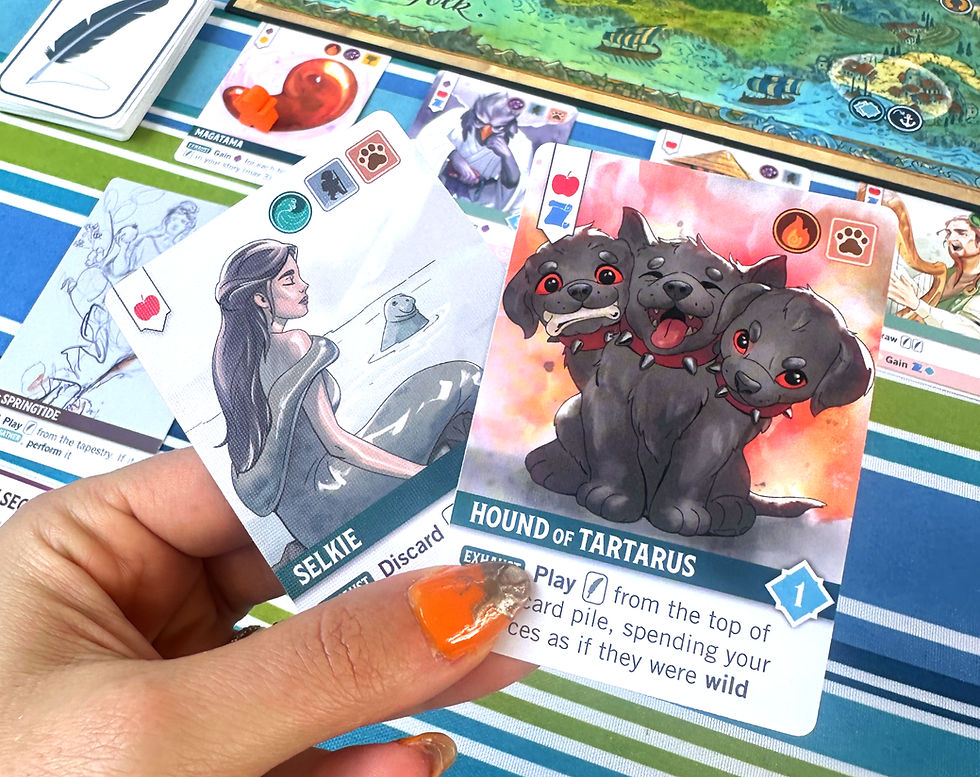 Cards of Selkie and Hound of Tartarus held over a striped tablecloth. Colorful board game elements and map visible in the background.