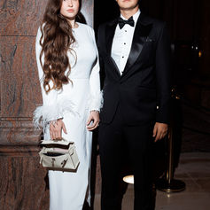 Two guests pose together in formal evening wear against the branded launch backdrop.