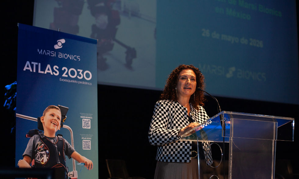 Mujer habla en un atril acrílico junto a un banner de MARSI BIONICS ATLAS 2030 en un auditorio oscuro.