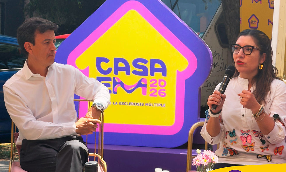 Dos personas conversan en un evento junto a un gran cartel morado y amarillo de CASA EM 2026 sobre esclerosis múltiple.