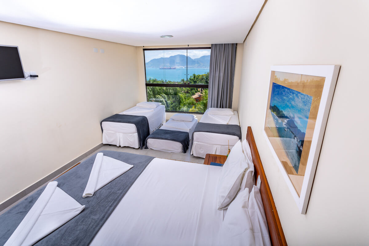 Suíte do Eco Baepi com uma cama de casal e três camas de solteiro, janela com vista para o mar e serra em Ilhabela