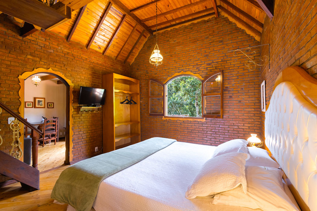 Quarto aconchegante com cama grande, lareira acesa e escada de madeira para mezanino na Estalagem Spiller em Monte Verde