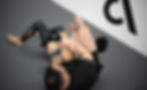 Two people on the ground practicing a jiu-jitsu technique. The person in the foreground is lying on their back, wearing a black t-shirt, and has a tattooed arm. Trein Fort Bend in Sugar Land, TX, USA
