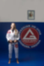 Professor Dana from the Gracie Barra Ashburn Jiu-Jitsu academy, with long blonde hair, wearing a white jiu-jitsu gi with red details and a black belt, is standing on a blue mat in a dojo in Virginia.