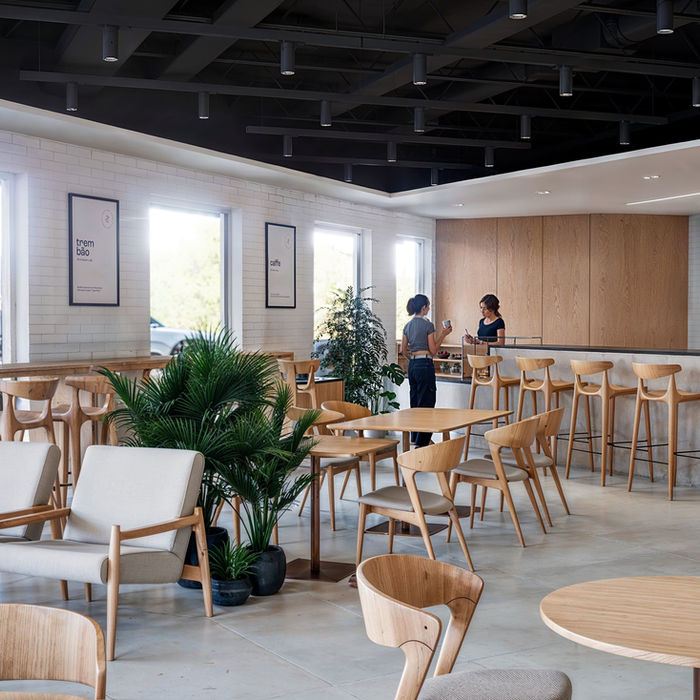 A modern and spacious café with several light wooden tables and chairs, along with upholstered armchairs in neutral tones, at Trein Club in Houston