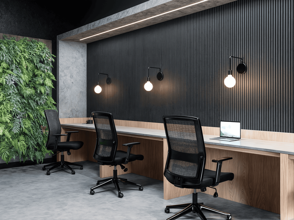 A modern workspace with three black mesh-back office chairs arranged in front of a long light wooden table with a gray top, at Trein Club in Houston