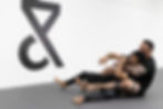 Two men on a jiu-jitsu mat, with one applying a chokehold or rear-naked choke on the other. Trein Fort Bend in Sugar Land, TX, USA