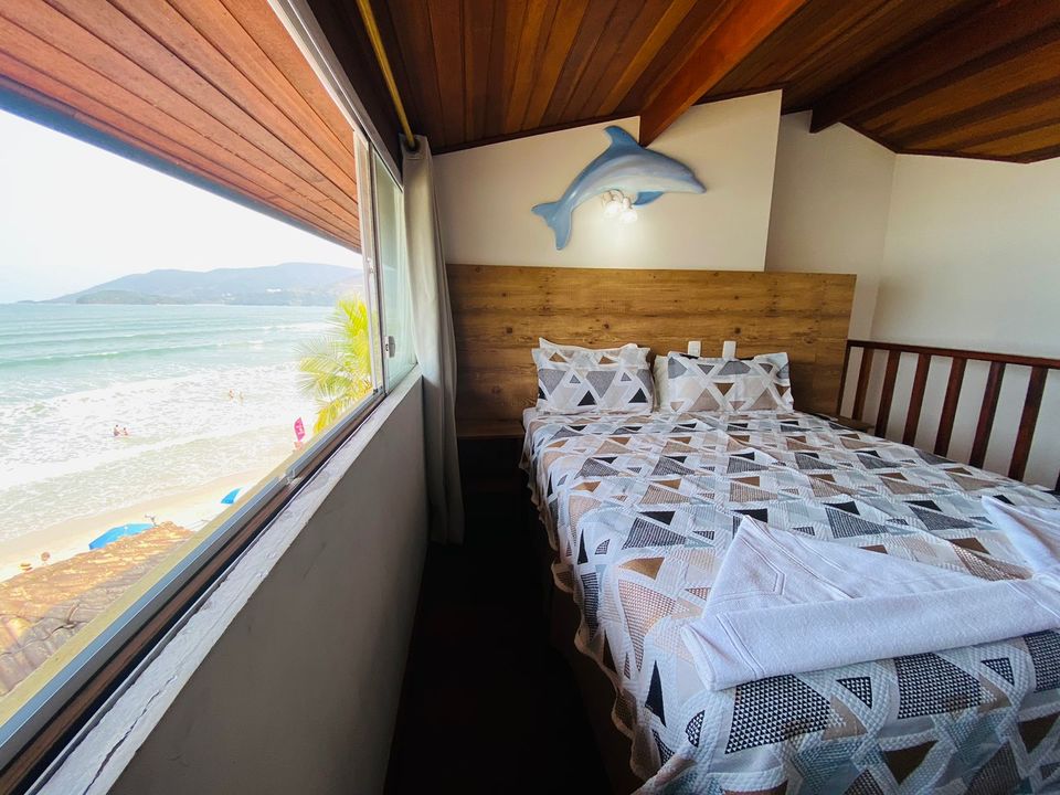 Suíte da Pousada Kaliman com cama de casal, decoração com golfinho e grande janela com vista para a praia de Ubatuba